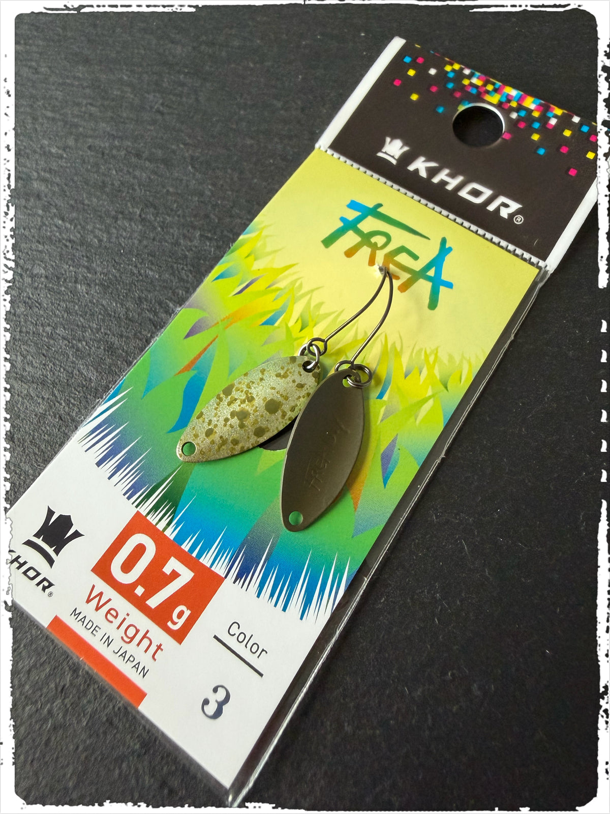 Khor Frea #FC03, 0,7 g: Löffelblinker (Vorder- und Rückseite) in Hellgrün-Beige gesprenkelt und Dunkeloliv auf Karte